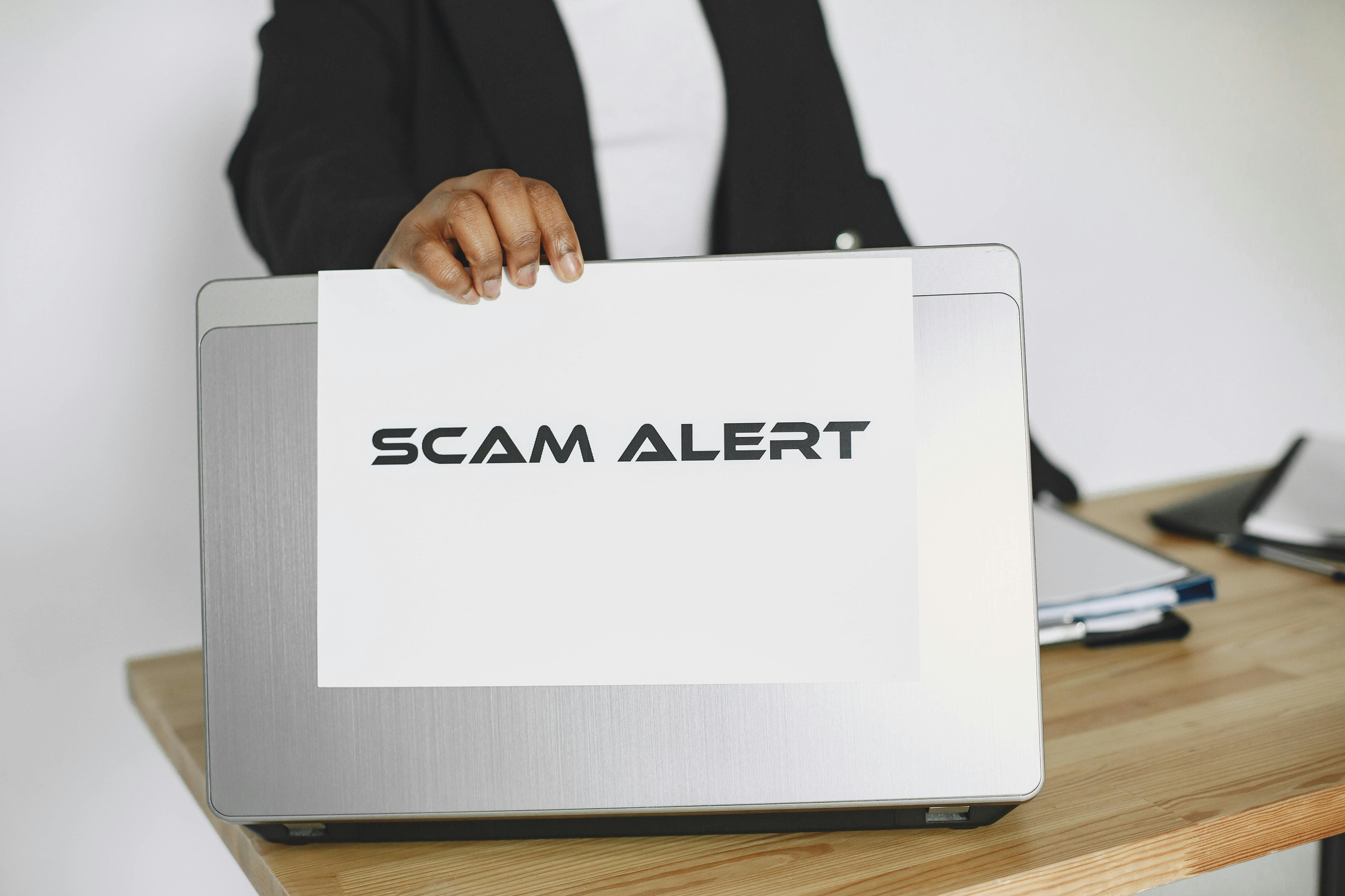 Letrero de scam alert sostenido frente a una laptop